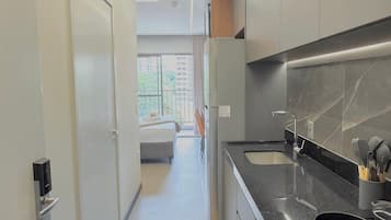A modern kitchen with a black countertop, stainless steel appliances, and a view to a balcony.