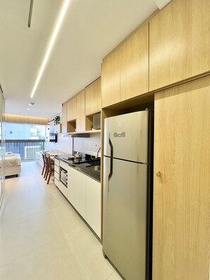 A modern kitchen with wooden cabinets, a stainless steel refrigerator, and a dining area with chairs. - La Vida (São Paulo)