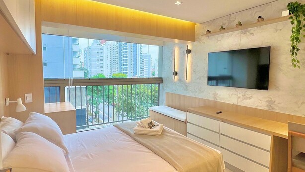 A modern bedroom with a bed, bedside table, TV, and a balcony with a city view. - La Vida (São Paulo)