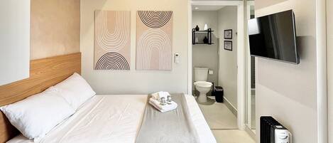 A modern hotel room with a bed, a TV, a heater, and artwork on the wall.