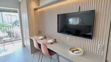 A modern kitchen with a built-in TV, wooden panel wall, and a dining area with pink chairs.