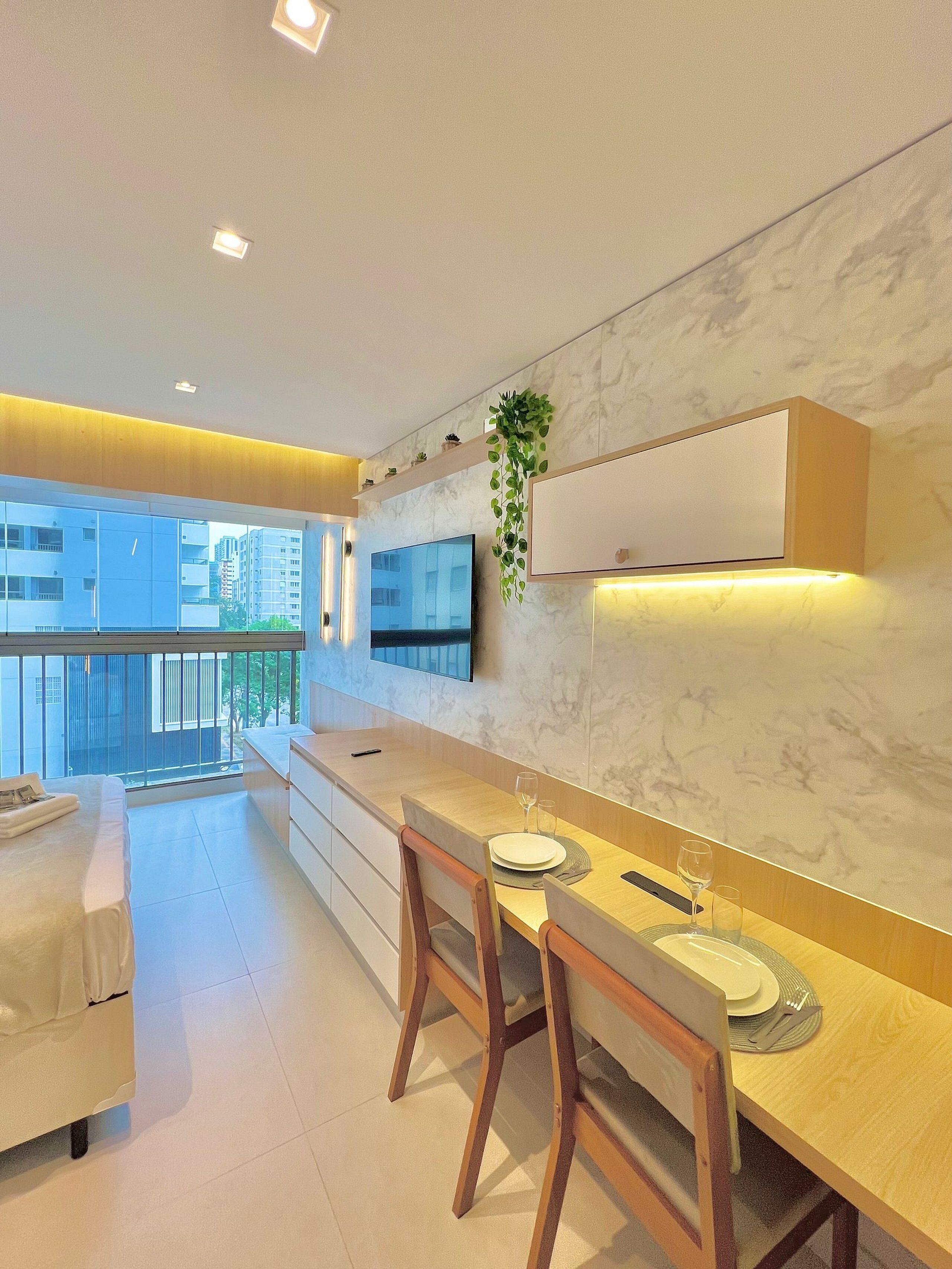 A modern kitchen with a large island, wooden chairs, a dining table, and a TV mounted on the wall.