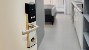 A modern hotel room with a minimalist design, featuring a sleek door with a digital lock, a small window, and a view of the balcony. - La Vida (São Paulo)