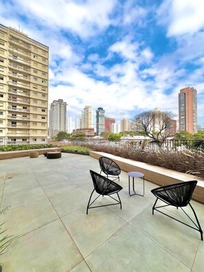 A rooftop terrace with two black chairs, a small table, and a view of surrounding high-rise buildings. - La Vida (São Paulo)