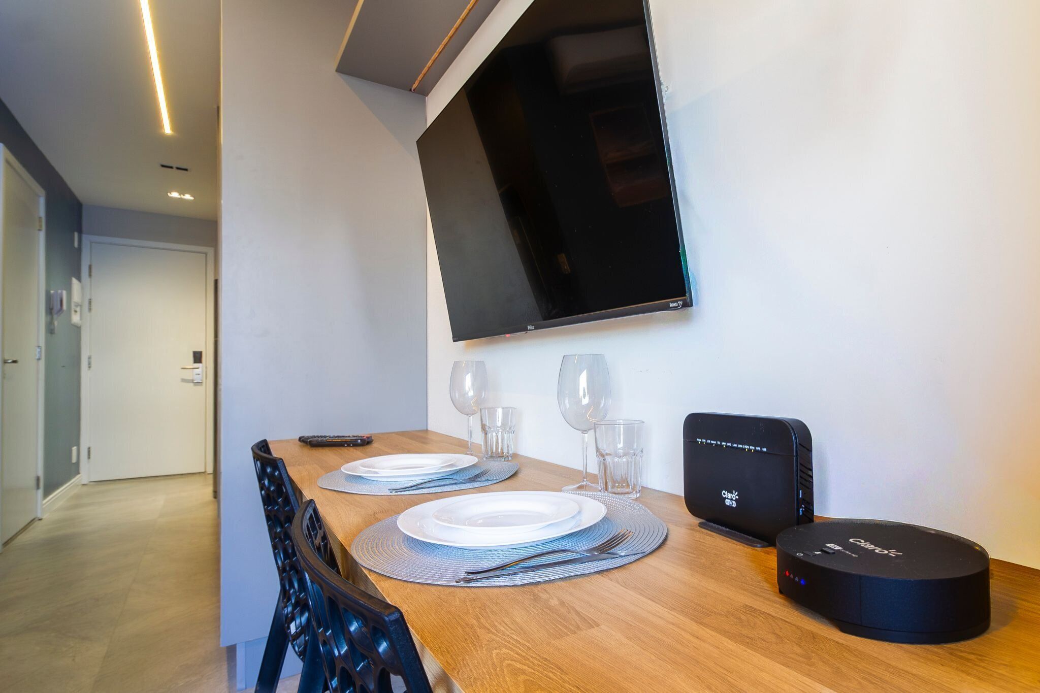 A dining area with a wooden table set for two, a flat-screen TV mounted on the wall, and a charging station on the table.