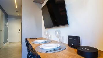 A dining area with a wooden table set for two, a flat-screen TV mounted on the wall, and a charging station on the table.