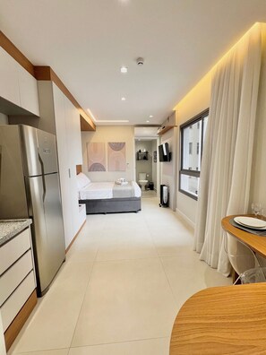 A modern hotel room with a kitchenette, a bed, a dining area, and a bathroom. - La Vida (São Paulo)