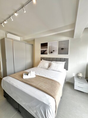 A modern hotel room with a large bed, a wardrobe, a bedside table with a lamp, and artwork on the wall. - La Vida (São Paulo)
