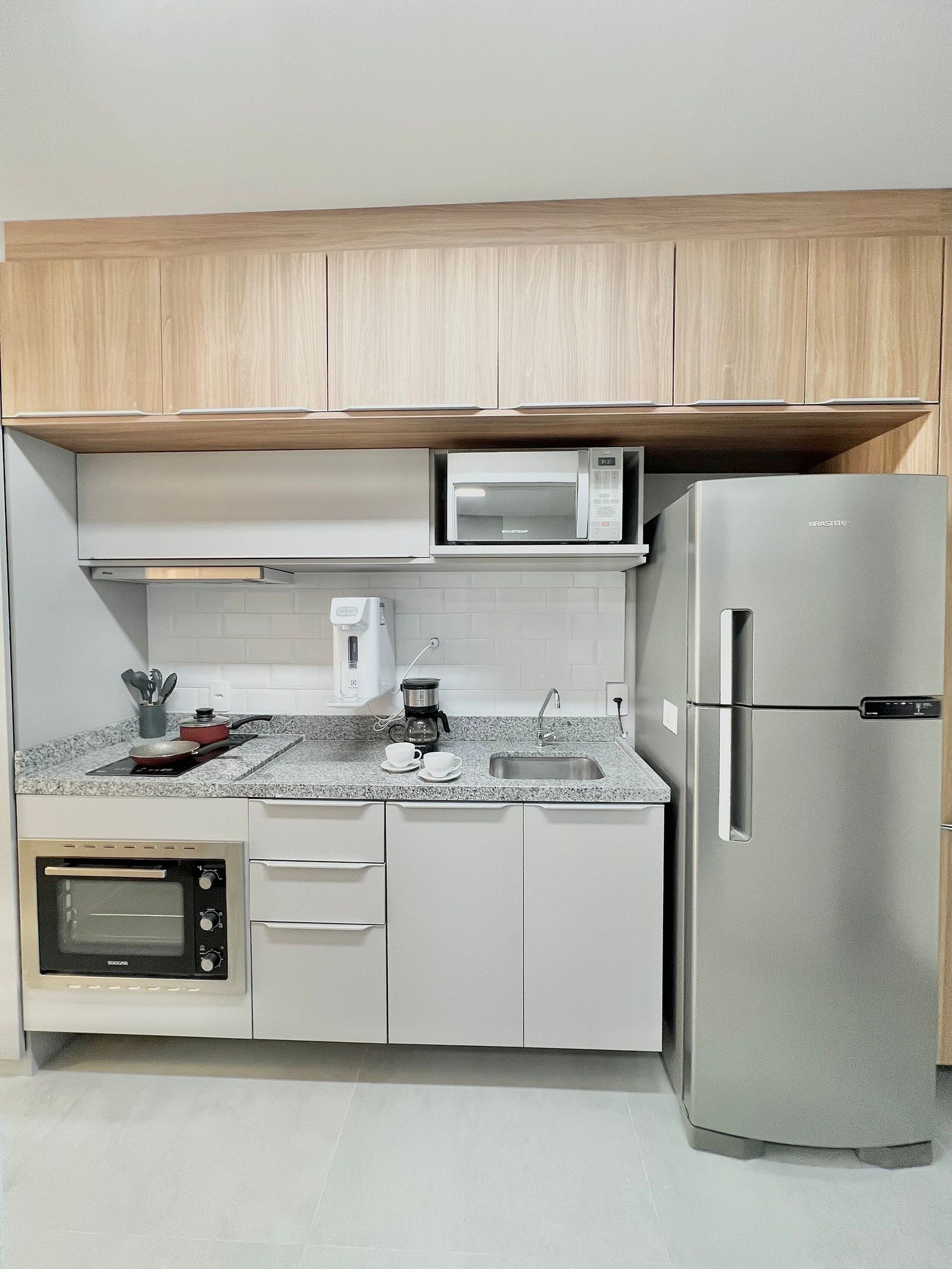 A compact kitchen with a built-in microwave, coffee maker, and a stainless steel refrigerator.