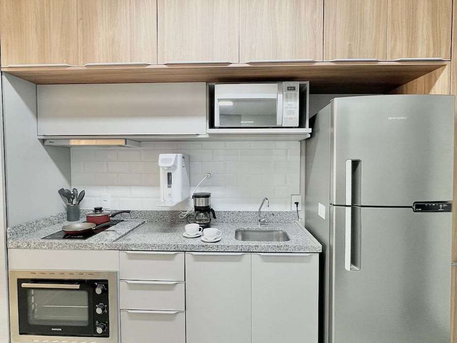 A compact kitchen with a built-in microwave, coffee maker, and a stainless steel refrigerator.