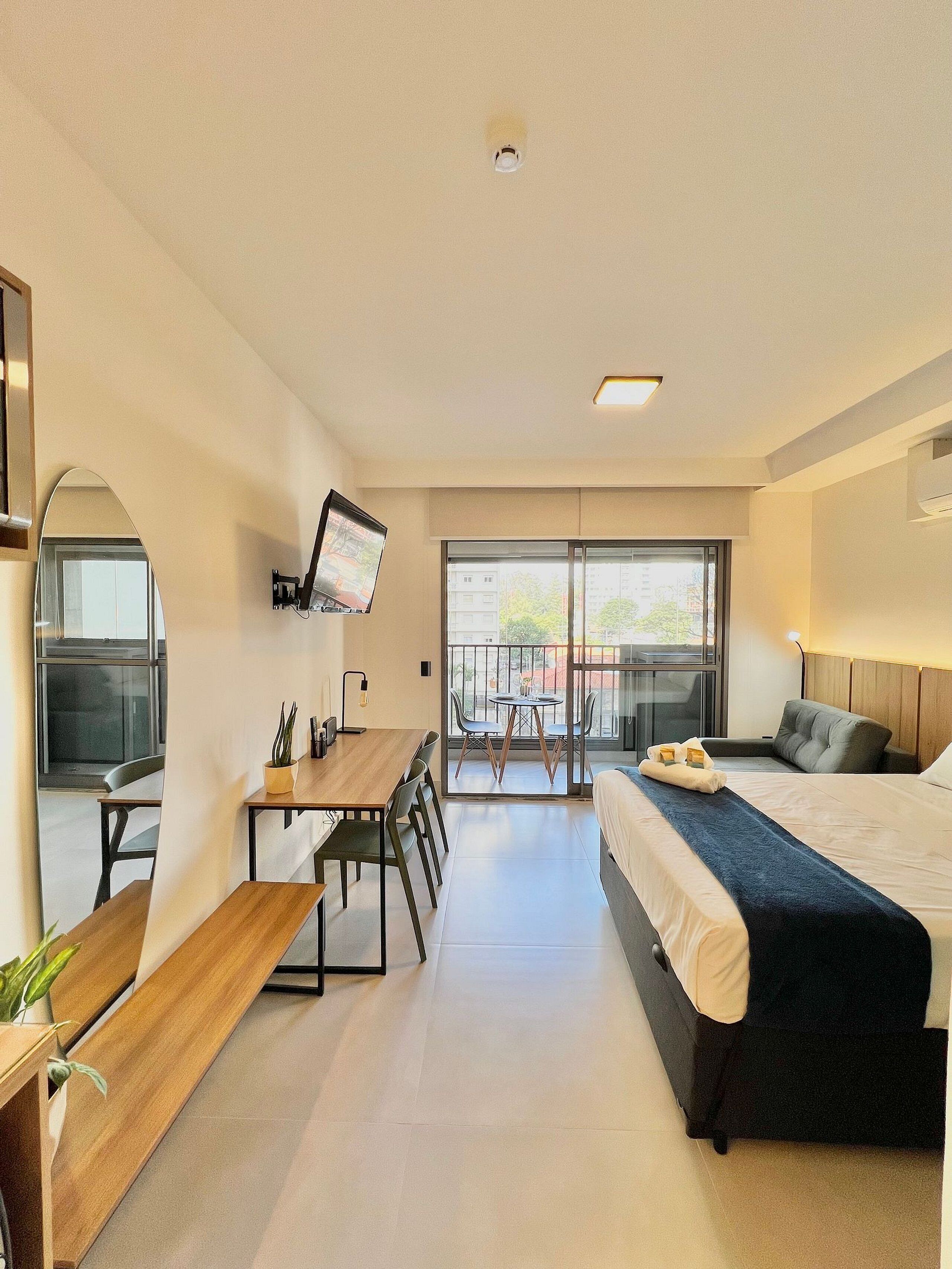 Une chambre d’hôtel moderne équipée d’un lit, d’un bureau, de chaises, d’une télévision et d’un balcon avec vue.