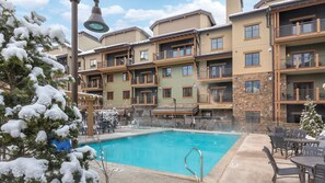 Un hotel de varios pisos con piscina, asientos al aire libre y árboles cubiertos de nieve.