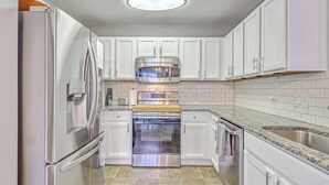 A kitchen with white cabinets, stainless steel appliances, a granite countertop, and a tiled backsplash. - Charming Charleston Escape (North Charleston)