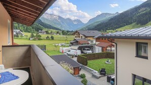Un balcon avec vue sur un paysage montagneux, un espace de stationnement et un bâtiment doté d’un toit en pente.