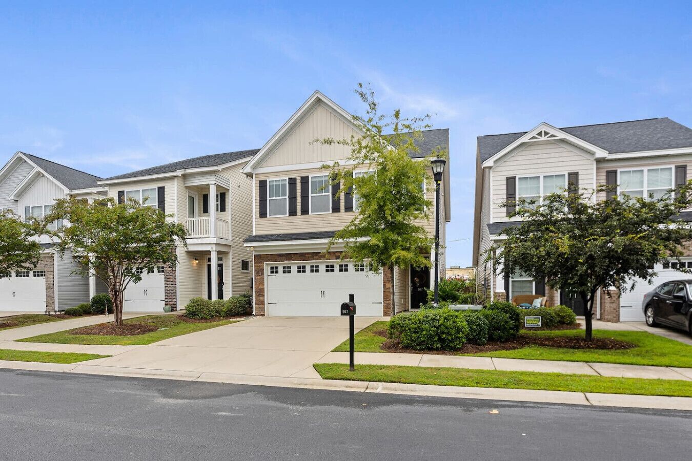 A row of two-story townhouses with attached garages, a central walkway, and small front yards with trees.