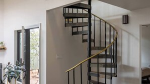 A spacious interior with a central spiral staircase, a balcony with a wooden railing, and a view of the outdoors.