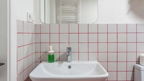 A bathroom with a white sink, red-tiled walls, a mirror, and a green plant. - Cozy studio with WiFi and AC in charming T'bilisi (T'bilisi)