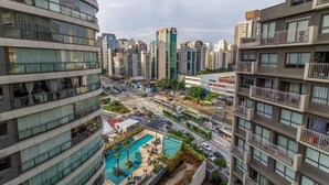 Un edificio de gran altura con varios balcones, una piscina y una calle concurrida con vehículos.