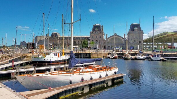 A marina with boats docked, a large building with a clock tower, and a covered walkway.