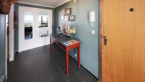 A hallway with a wooden door, a desk with a model ship, and a view through a door to a balcony.