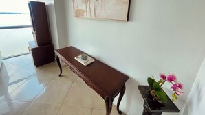 Una habitación con una mesa de madera, un cuadro abstracto enmarcado, un florero con flores y vistas al exterior por una ventana.