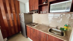 Cocina compacta con armarios de madera, un refrigerador de acero inoxidable, microondas y pileta con escurreplatos.