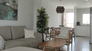 Ein modernes Wohnzimmer mit einer Couch, einem Esstisch und Stühlen. An der Wand hängt ein großes Gemälde und eine Topfpflanze steht dort.
