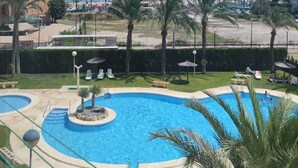 Ein Poolbereich mit Palmen, Liegestühlen und Blick auf Strand und Meer.