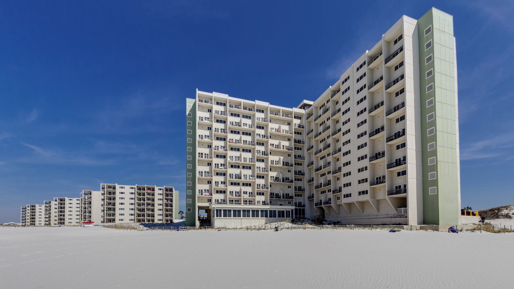 A beachfront hotel with multiple floors, balconies, and a sandy beach in the foreground.