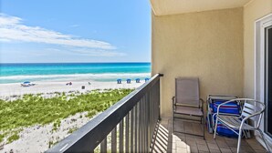 Ein Balkon mit Blick auf den Strand, ein Stuhl und ein Stapel zusammengeklappter Stühle.