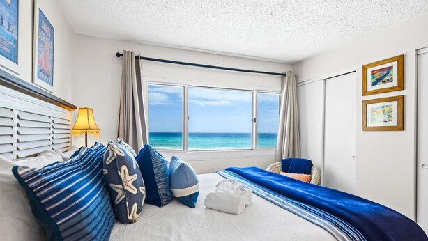Ein Hotelzimmer mit Bett, Fenster mit Meerblick, Lampe und Stuhl.