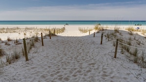 Ein Sandweg am Strand, der zum Meer führt, mit einem Seilzaun und Holzpfählen.