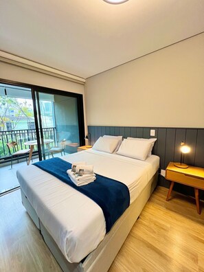 Une chambre d’hôtel moderne avec un grand lit, une table de chevet avec une lampe, un balcon avec des chaises et une vue sur la ville.