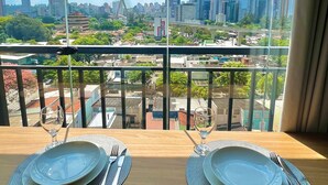 A dining table with plates and cutlery, set against a cityscape view through a window. - Innvista -Trends Brooklin. (São Paulo)