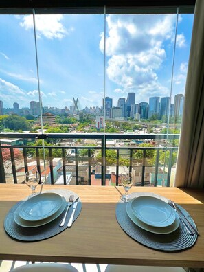 Uma mesa de jantar com pratos e talheres, com vista para a cidade através de uma janela.