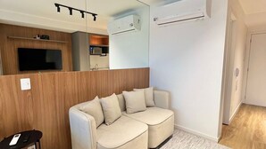 A modern living room with a sectional sofa, a small table, and a kitchen area in the background. - Innvista -Trends Brooklin. (São Paulo)