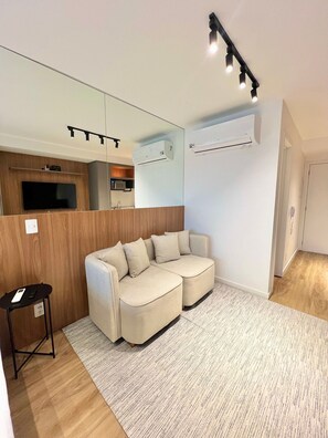 Uma sala de estar moderna com um sofá modular, uma mesinha e uma cozinha ao fundo.