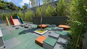 Un giardino pensile con zone relax, un piccolo albero e un'area giochi.