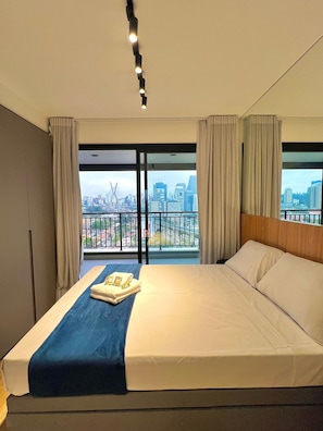 A hotel room with a large bed, a view of the cityscape through the windows, and a balcony with a railing. - Innvista -Trends Brooklin. (São Paulo)