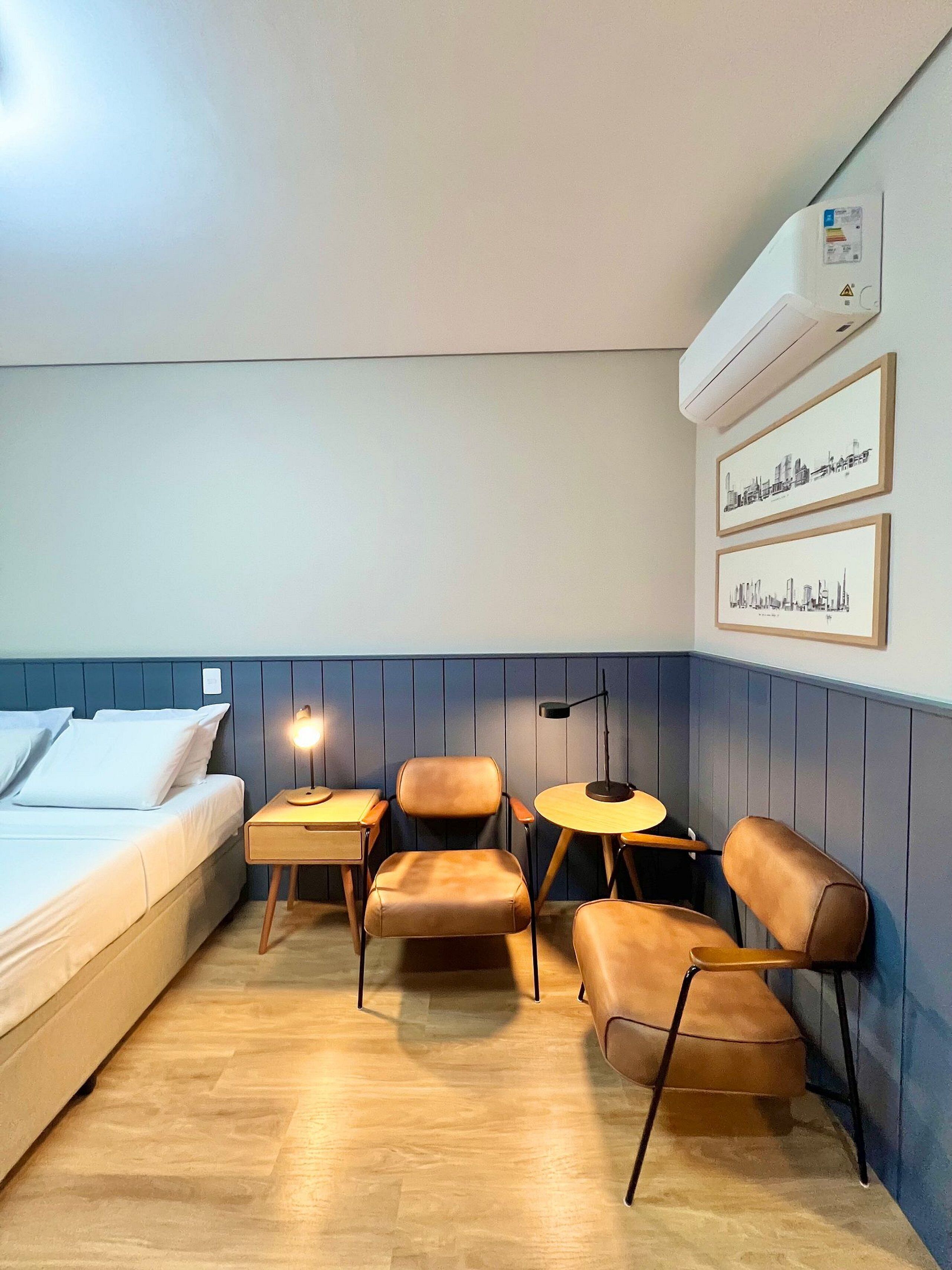 A hotel room with a bed, a desk, two chairs, a small table, and wall-mounted air conditioning.