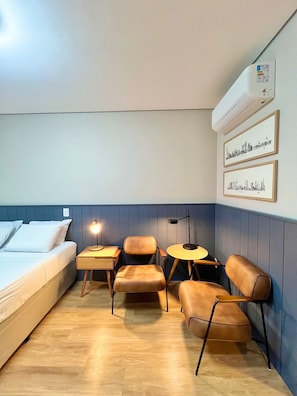 A hotel room with a bed, a desk, two chairs, a small table, and wall-mounted air conditioning. - Innvista -Trends Brooklin. (São Paulo)
