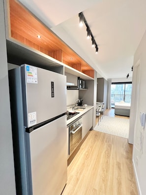 A modern kitchen with a built-in refrigerator, microwave, and oven. There is a dining area with a table and chairs, and a large window providing a view of the city. - Innvista -Trends Brooklin. (São Paulo)