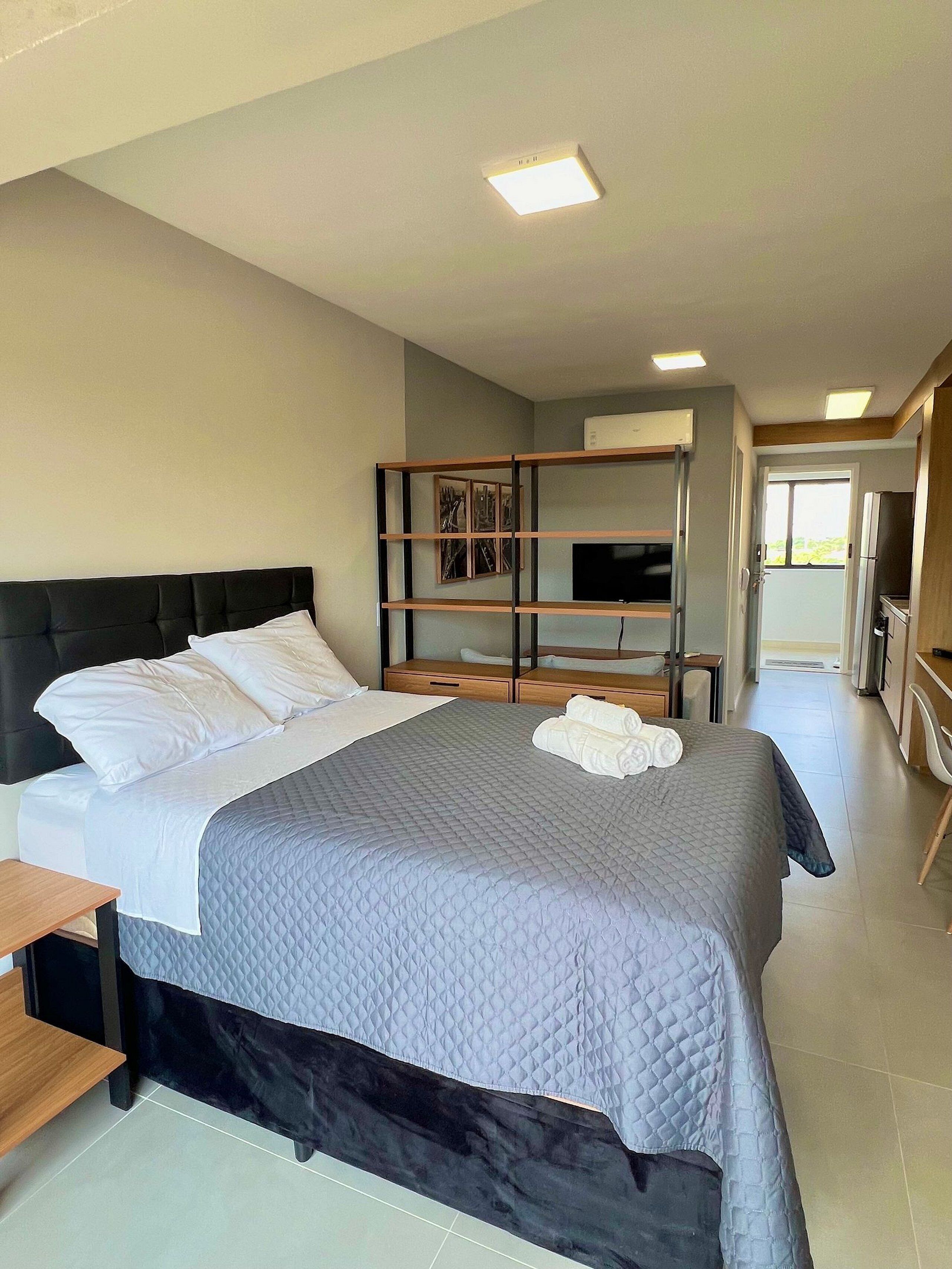 A modern hotel room with a large bed, a TV, a wardrobe, and a bathroom visible through an open door.