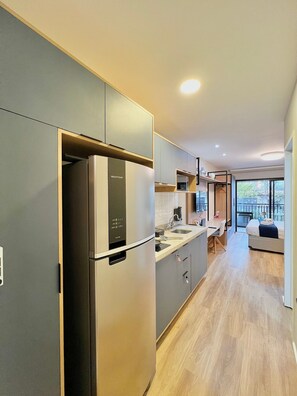 Eine moderne Küche mit integriertem Kühlschrank, Mikrowelle und Spüle. Ein Essbereich mit Tisch und Stühlen sowie ein Bett mit Blick aus dem Fenster.