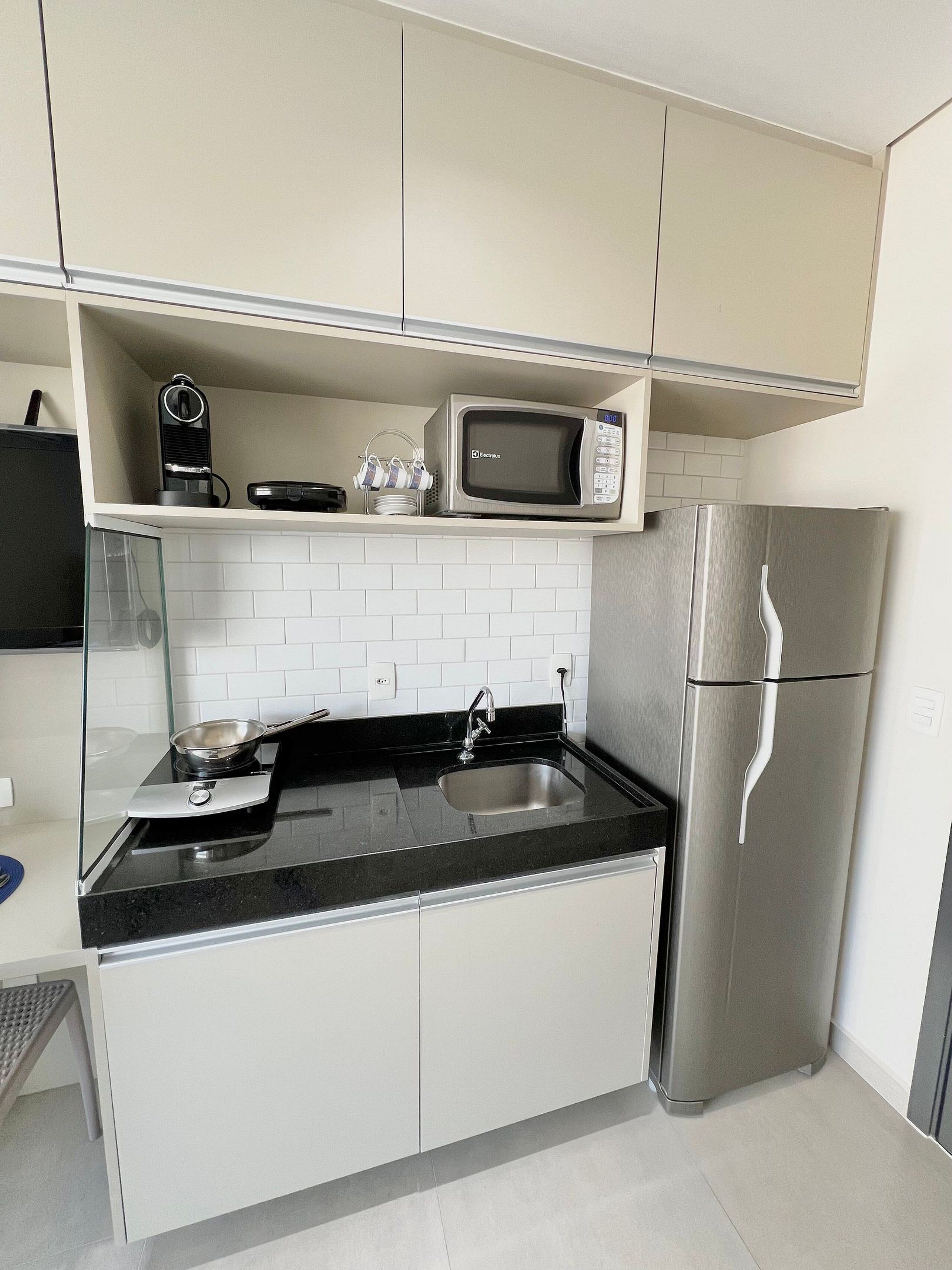 A modern kitchen with white cabinets, a stainless steel refrigerator, a microwave, and a black countertop.