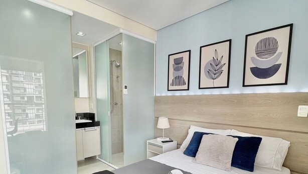 A modern bedroom with a large bed, a bedside table with a lamp, and a wall with three framed artworks. - VN Quatá (São Paulo)
