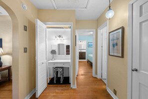 Un couloir avec une porte blanche, un miroir, un tapis à motifs zébrés et, au fond, un lit.