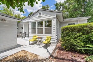 Une maison blanche avec une grande fenêtre, un patio avec deux chaises et un jardin bien entretenu.