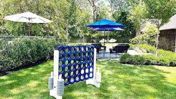 Patio trasero con una estructura de juego azul y blanca, dos sombrillas y un área de descanso con sillas y una mesa.