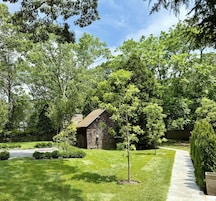 A well-maintained garden with a wooden cabin, a small tree, and a paved pathway.